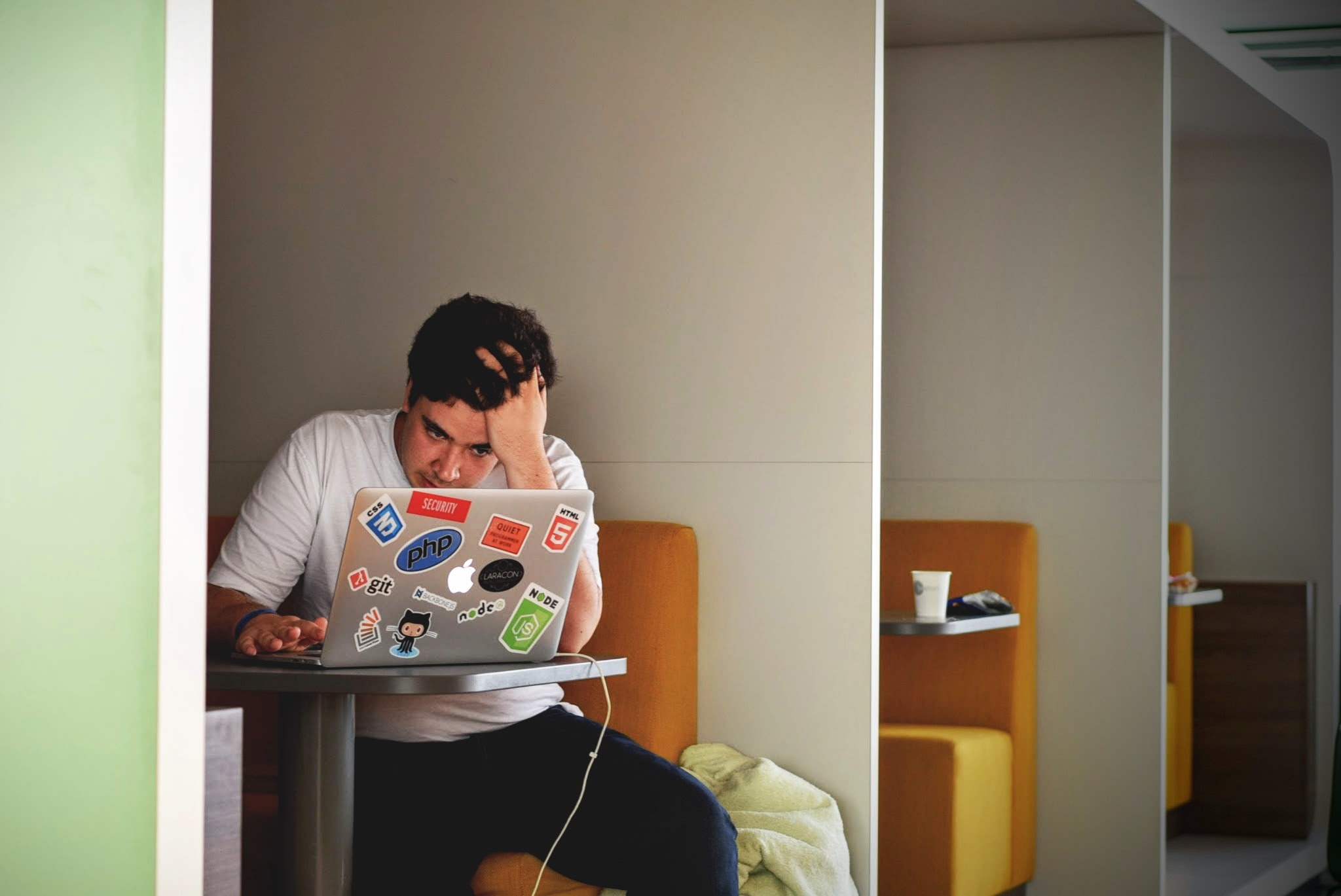 Homem sentado a frente de um notebook, o qual possui muitas figurinhas de tecnologias diferentes.